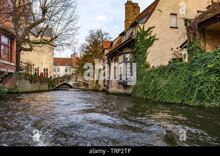 Picturesque old street of Bruges with traditional medieval houses, ivy, canal and bridges. Cityscape of Bruges streets shot from the boat. Stock Photo