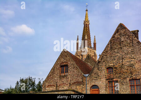 The Church's of Our Lady (Onze-Lieve-Vrouwekerk) tower seen behind medieval houses against blue sky. This Gothic tower is 122.3 metres high Stock Photo