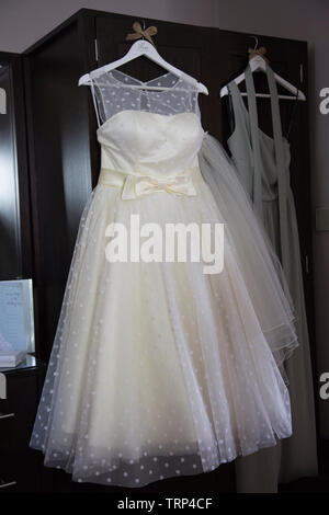 Brides white wedding dress hanging up waiting to be worn on her wedding day, before her wedding ceremony Stock Photo