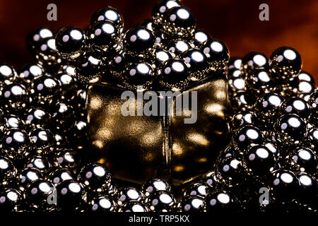 very industrial feeling golden colored magnetic cube surrounded by many tiny steel ball bearings.  The reflections in each ball are very detaileed Stock Photo