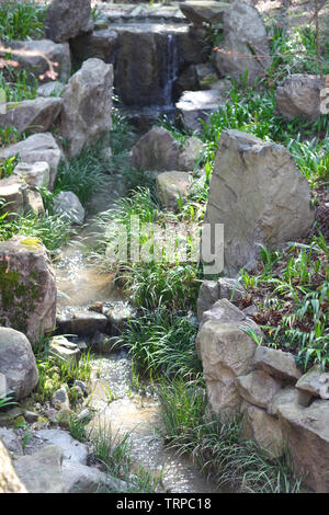 A small waterfall and stream flowing among grass and stones in traditional Japanese garden Stock Photo