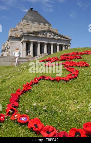 Vertical image of red yarn poppies, winding up small hill, on green grass with blue sky and Shrine of Remembrance in background on Armistice Day. Stock Photo