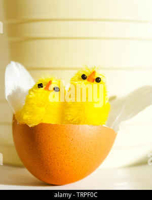 Two Easter chicken decorations in an egg shell on a light yellow background. Stock Photo