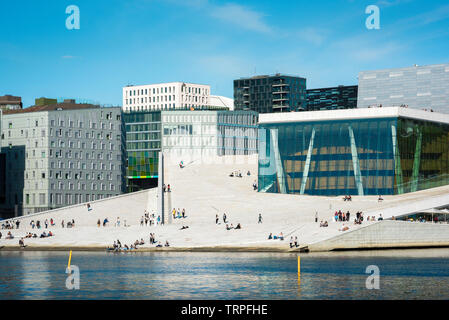 Opera House Oslo, view across Oslofjord of people on the vast access ramp leading to the roof of the Oslo Opera House, with Barcode Buildings beyond. Stock Photo