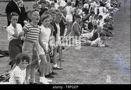 1955, historical, at a primary school sports day, young children line the field behind a rope cheering and encouraging their fellow pupils taking part in the events, England, UK. Stock Photo