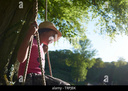 Asian mother and her young daughter having fun playing on a swing hanging on a large tree in front of a castle in bright summer sunshine