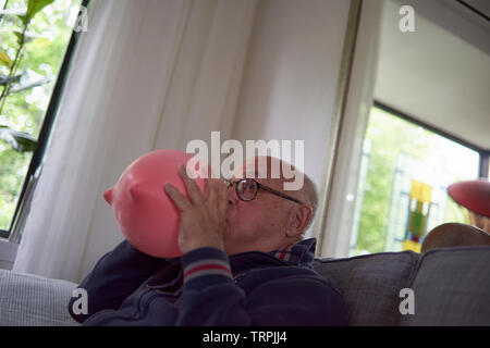 Elderly retired man blowing up a large heart shaped pink balloon to decorate the room for a birthday party Stock Photo