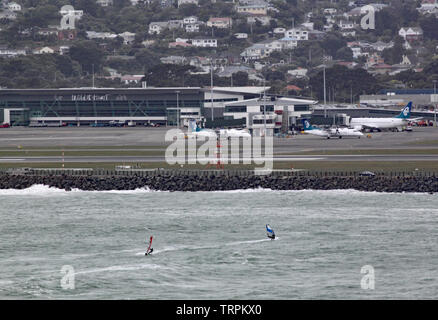 Two wind surfers on Lyall Bay in Wellington New Zealand on a grey stormy day. The airport can be seen in the background. Stock Photo