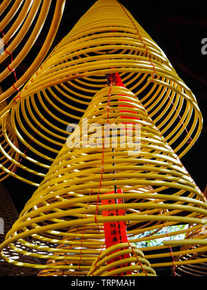 Multiple large yellow incense coils hanging in stacks from the ceiling in a Chinese temple Stock Photo