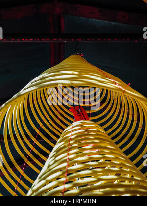 Multiple large yellow incense coils hanging in stacks from the ceiling in a Chinese temple Stock Photo