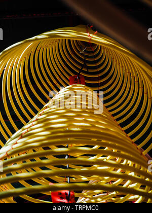 Multiple large yellow incense coils hanging in stacks from the ceiling in a Chinese temple Stock Photo