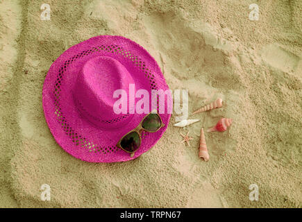 Shocking pink straw hat with sunglasses and many little seashells on the sandy beach for holiday concept Stock Photo