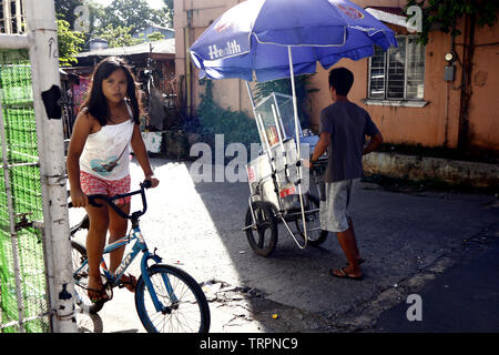 A young Filipino girl riding a bicycle with another child within a slum ...