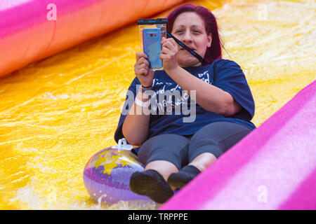 Woman on inflatable ring having fun and taking selfie on giant waterslide, water slide, at Bournemouth, Dorset UK in June Stock Photo