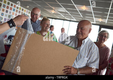 A group of elderly retired friends celebrating a 50th wedding anniversary at a restaurant with the happy couple unwrapping presents Stock Photo