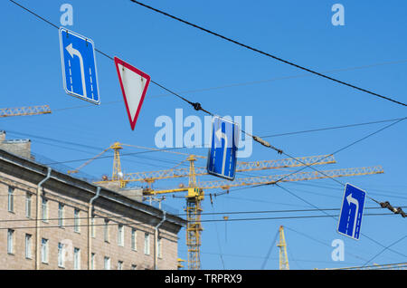 Road signs 'turn left' and 'give way' in the background construction cranes and blue sky Stock Photo