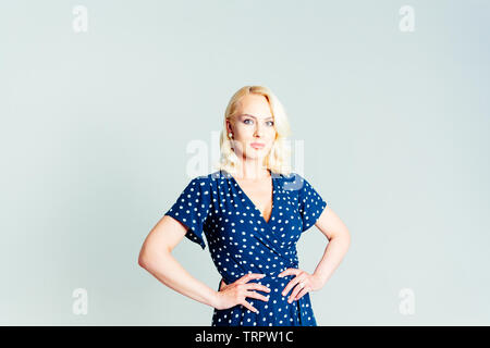 Studio portrait of beautiful blonde woman in a dark blue dress against white plain background Stock Photo