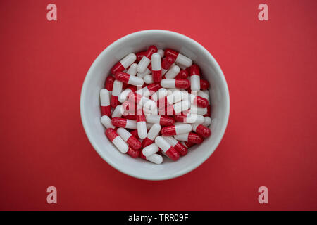 Bowl of drugs pills capsules on red color background Stock Photo