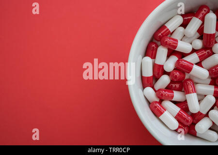Bowl of drugs pills capsules on red color background Stock Photo