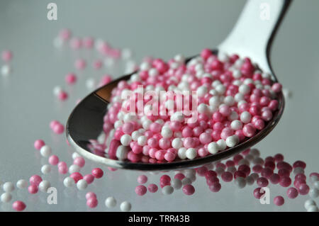 macrophotography of pink and white sugar pearls in a tea spoon on glass plate Stock Photo