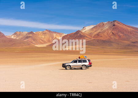 Two 4x4 cars wait in the Siloli desert with the colourful Andes in the background in the Altiplano region of Bolivia. Stock Photo