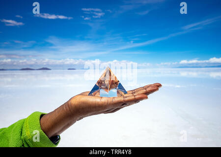 Hand holding a crystal pyramid in front of a wide and sunny salt desert Stock Photo