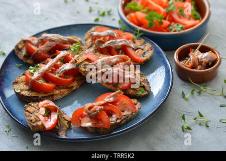 Spanish bar food: Grilled slices of bread with olive oil, herbs, fresh tomatoes and spicy anchovy fillets Stock Photo