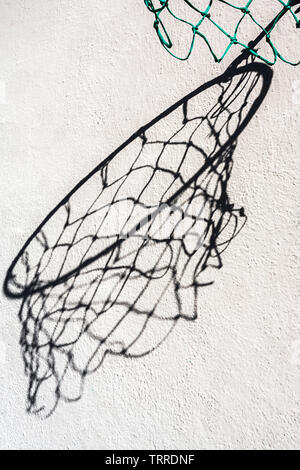 Abstract view of a hoop and net casting a large distorted shadow on a wall. Stock Photo