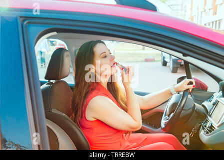 Side view young woman looking in rear view mirror and putting make up in car. Modern busy life. beautiful girl sitting in drivers seat of car applying Stock Photo