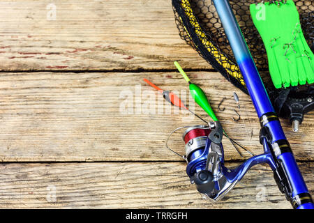Fishing tackle. Fishing rod, floats, fishing hooks and landing net on old wooden background with free space for text. Stock Photo
