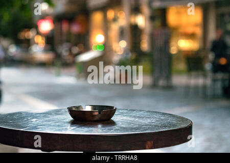 A bar round wooden table with an ashtray, outdoors in the evening, copy space. Stock Photo