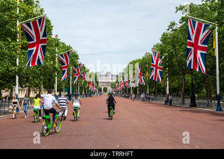 London, England, UK - June 1, 2019: Tourists ride electric hire bikes along The Mall in central London, with Union Jack flags flying. Stock Photo