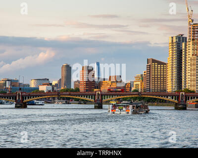 London, England, UK - May 28, 2019: A ferry boat passes under Vauxhall Bridge on the River Thames with the cityscape of Lambeth riverside behind. Stock Photo