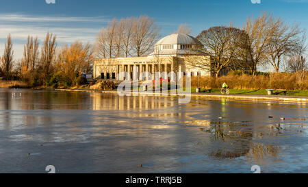 Newcastle, England, UK - February 6, 2019: A cyclist rides past the art deco Palace of Arts building and frozen lake on a winter day in Exhibition Par Stock Photo