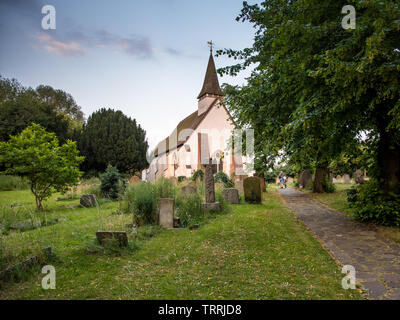 London, England, UK - June 18, 2017: A man pushes a bicycle through the churchyard of the 13th Century St Mary The Virgin church in Northolt, west Lon Stock Photo