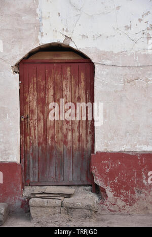 Red door on a whitewashed adobe brick wall. Ayacucho, Peru Stock Photo