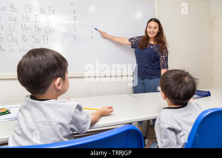 Manila, Philippines - August, 18, 2016: A female English teacher teaching two little boys, explaining ABC alphabet on board in classroom at school Stock Photo