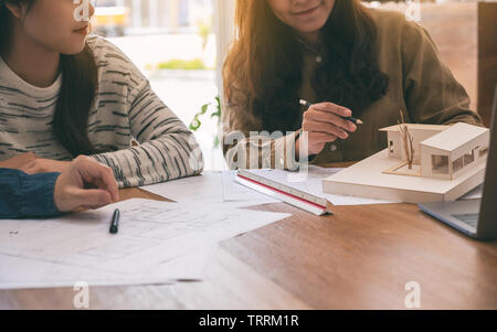 Group of an architect holding and discussing about an architecture model with shop drawing paper on table in office Stock Photo