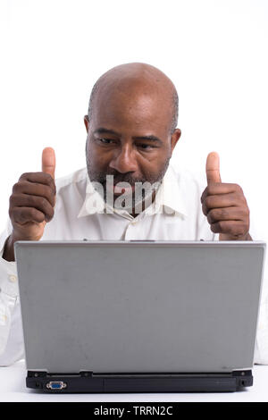 Portrait of a confident African American software expert signaling ok with thumbs up while sitting front of a laptop computer.   Happy man working. Stock Photo