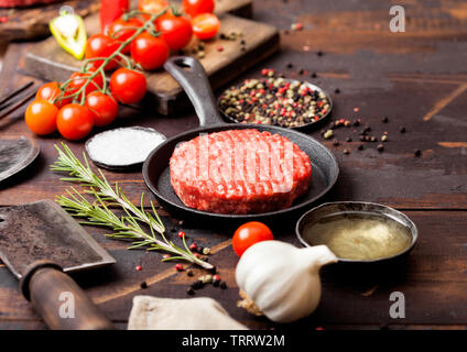 Fresh raw minced homemade farmers grill beef burger in frying pan with spices and herbs and meat hatchet on wooden board.