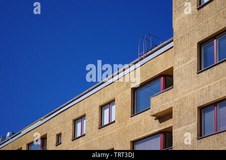 Brown apartment building exterior red frame windows with handrail on the roof and blue sky Stock Photo