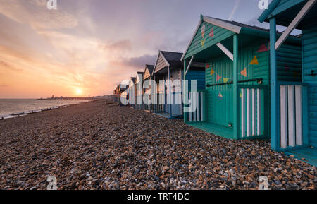 Colourful beach huts on Herne Bay seafront as the sun rises over the historic pier. Stock Photo