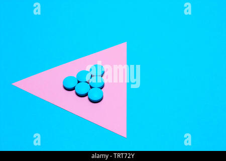 blue tablets laid out in the form of a triangle or an arrow on a paper background of blue and pink. Medication and prescription pills minimalistic fla Stock Photo
