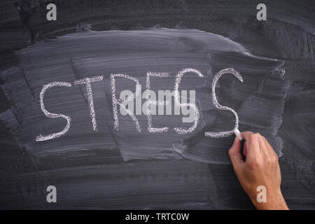 Person writing the word Stress on a blackboard. Close up. Stock Photo
