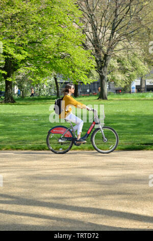 Young woman riding hired bicycle in Hyde Park, London, United Kingdom Stock Photo