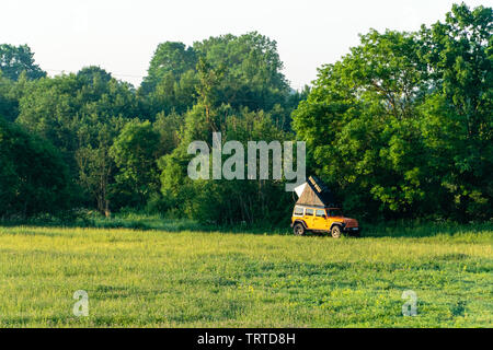 Jurgaiciai, Lithuania - 8 JUNE 2019: Orange SUV Jeep Wrangler with rooftop tent parked in meadow next to river Stock Photo