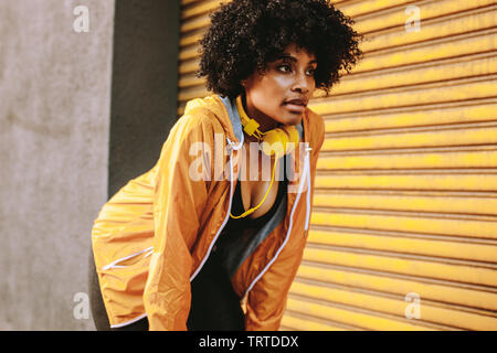 fitness woman relaxing with hands on knees during workout standing outdoors. African woman in sportswear taking rest while training outdoors. Stock Photo