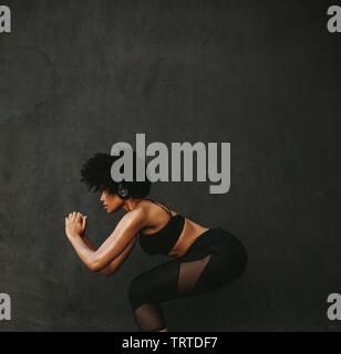 Young athletic woman exercising squats against a grey wall. Fit woman doing squats outdoors in morning. Stock Photo