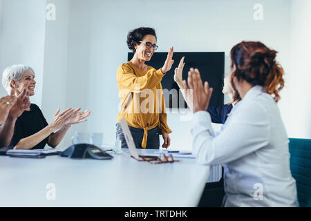 Happy business team in casual clothes at conference table  giving high fives to each other, celebrating success. Business team starting a new project. Stock Photo