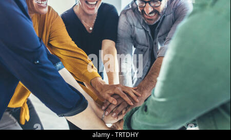 Multi-ethnic business people putting their hands on top of each other. Business team making a stack of hands showing unity. Stock Photo